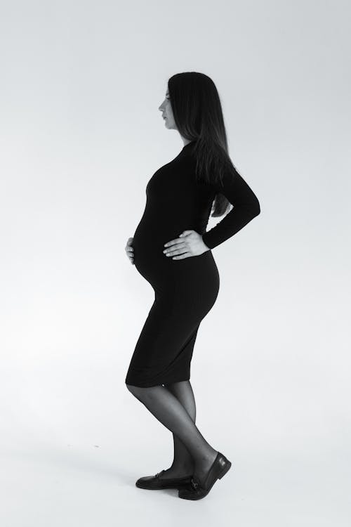 Free Pregnant Woman in Black Long Sleeve Dress Holding Hand on Belly Stock Photo