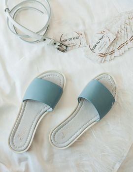 A stylish flat lay featuring blue sandals and white leather belt on a white background.