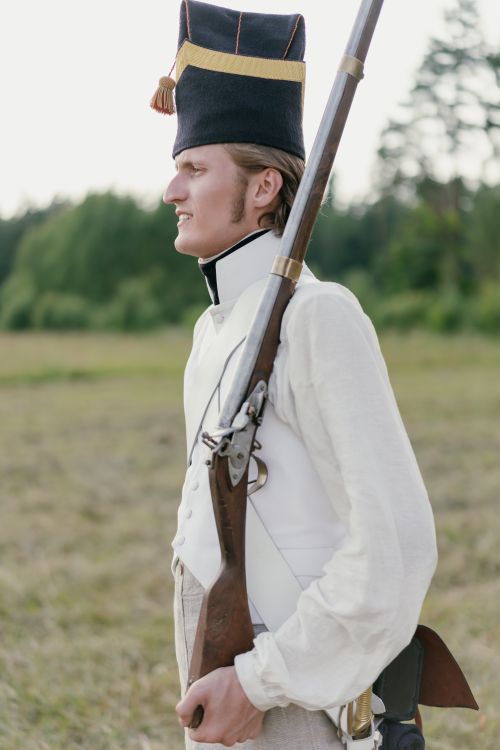Free A soldier in historical uniform stands with a rifle in a field during reenactment. Stock Photo