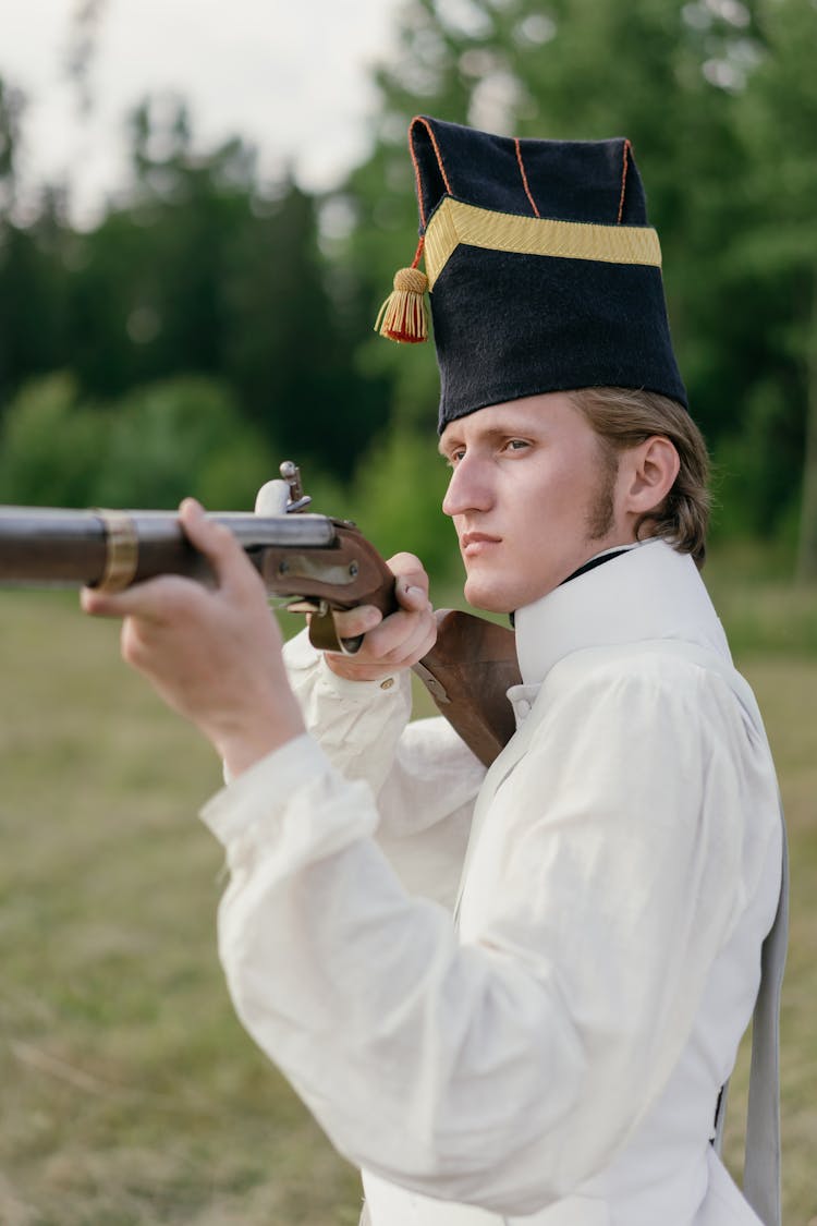 A Man In White Uniform With Black Hat Holding Rifle