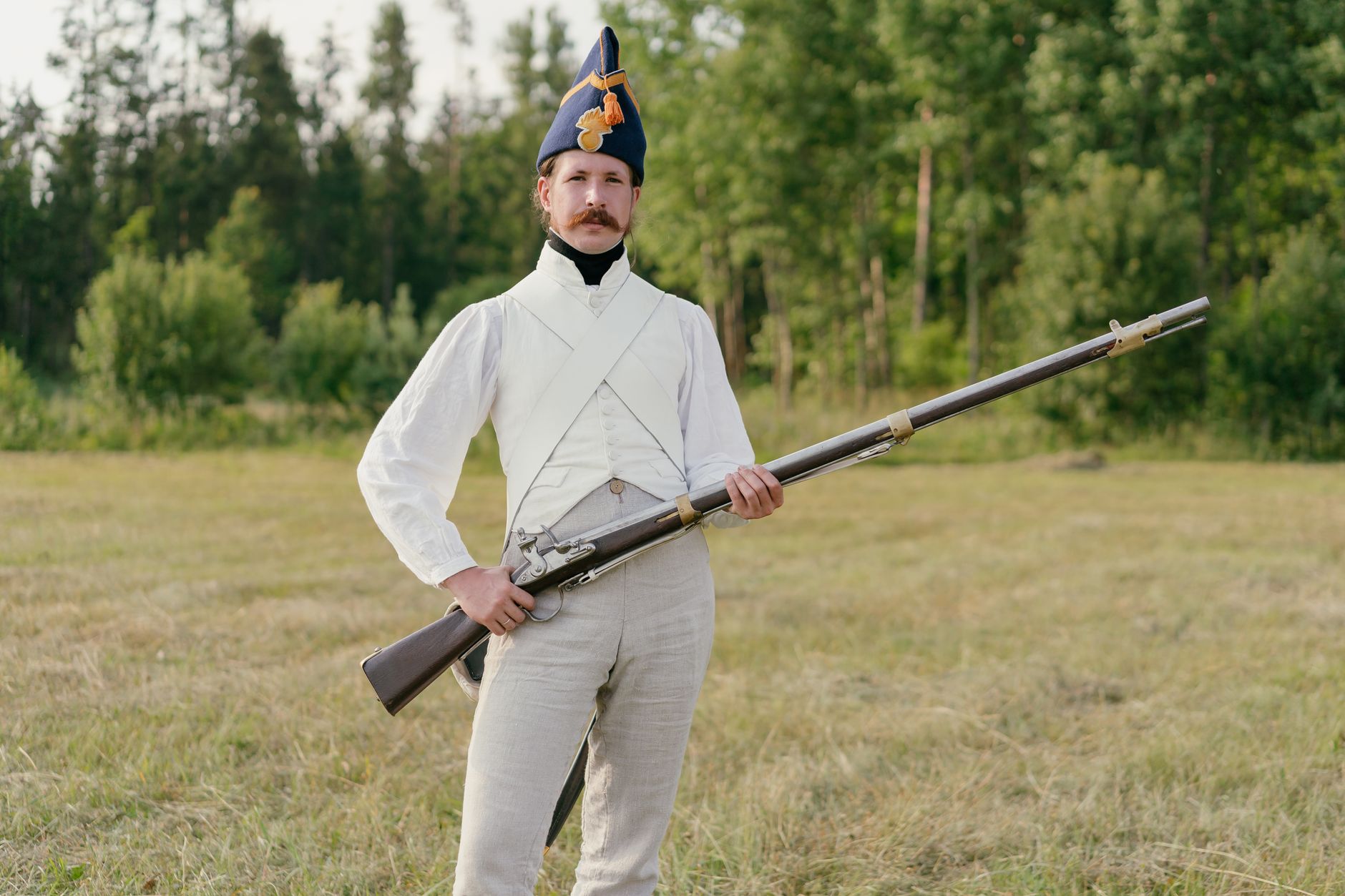 Man dressed in historical uniform with musket in a field setting.