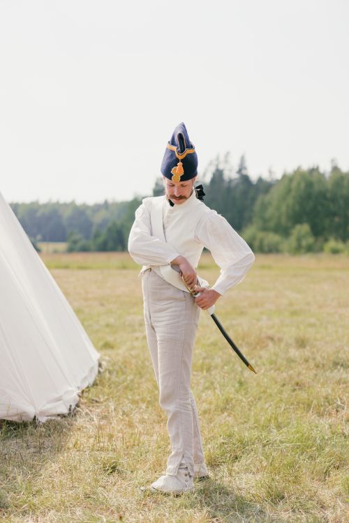Free A soldier in historical uniform adjusts their sword during a military reenactment outdoors. Stock Photo