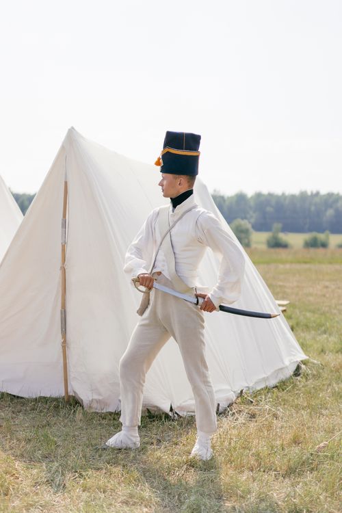 Free Man in historical uniform with saber standing by tents in field. Stock Photo