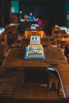 Vintage classroom setting featuring wooden desks and a stack of classic books in focus.