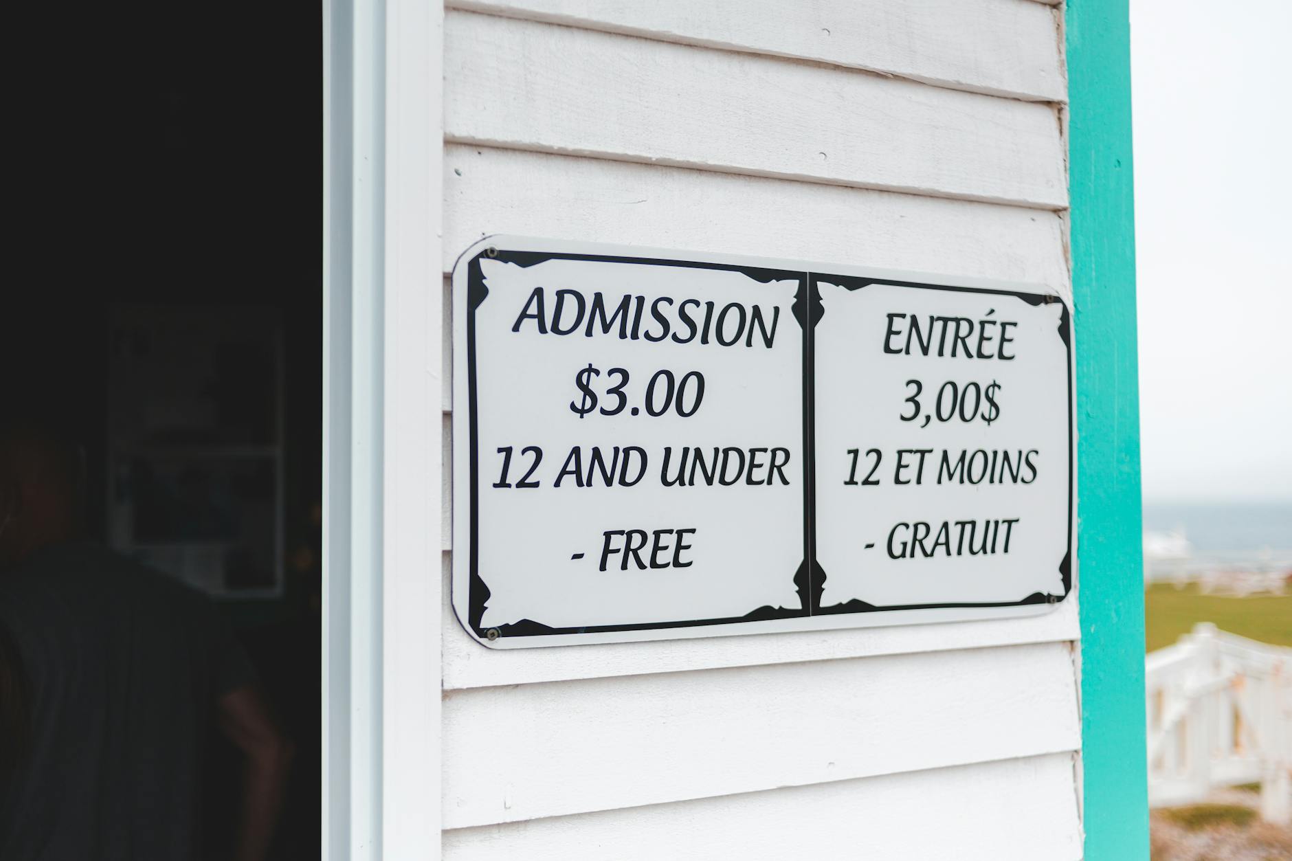 Bilingual sign displaying admission prices in English and French at building entrance.