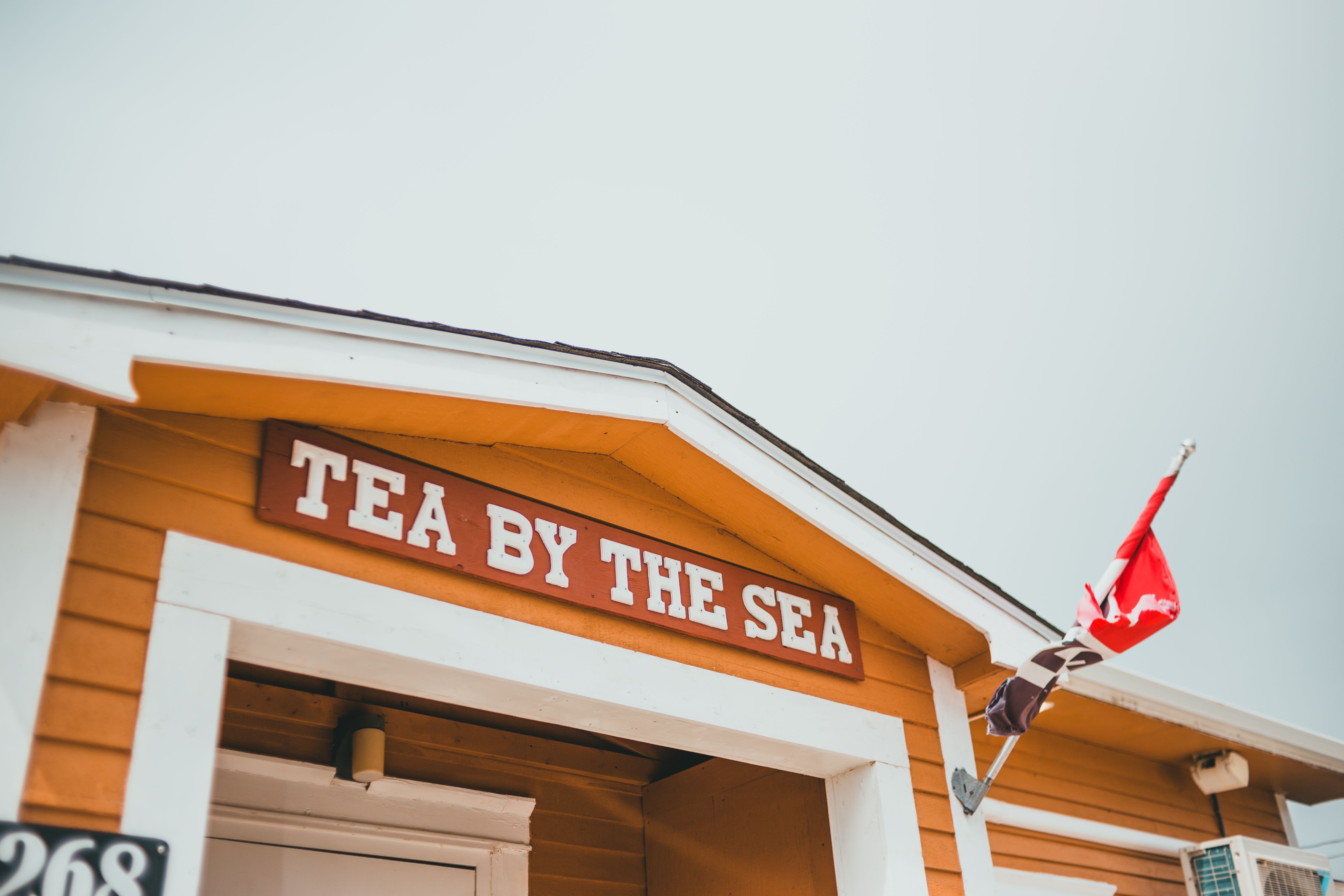 Bright wooden tea shop with 'Tea By The Sea' sign and flag, captured outdoors.