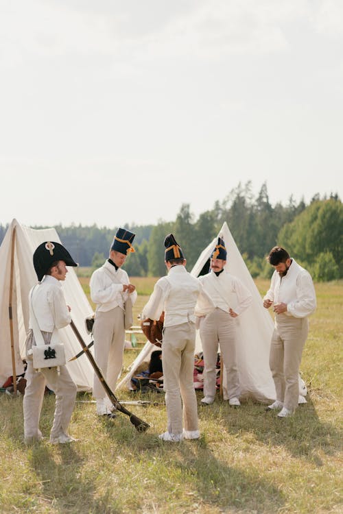 Free Men in French military uniform standing during reconstruction on grassy ground near tents and trees in countryside Stock Photo