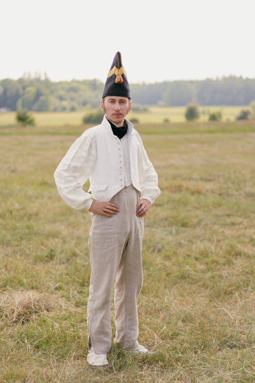 Soldier in a Historical Uniform Standing in the Grass Field with his Hands on Hips 