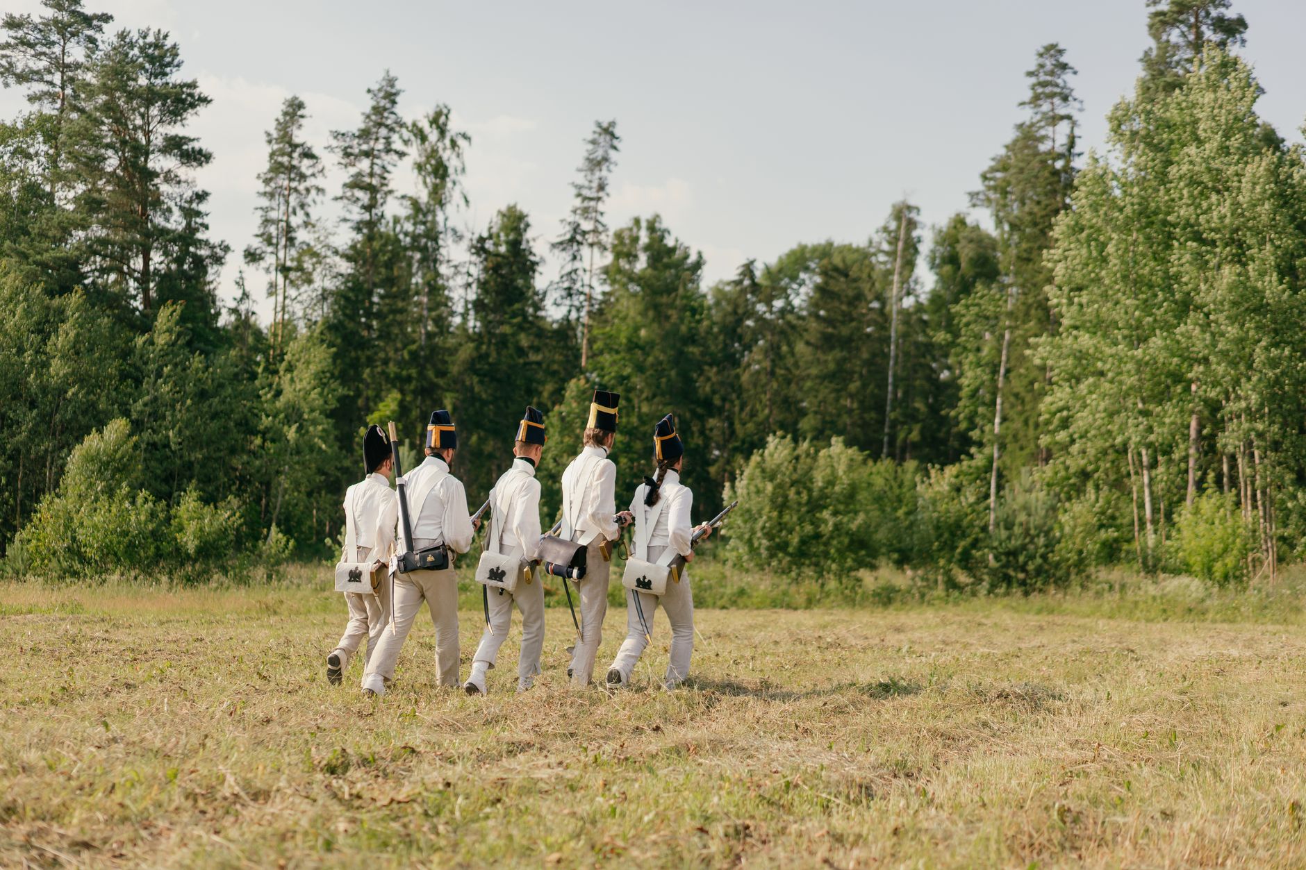 Group of soldiers in historical uniforms marching through a forest clearing.