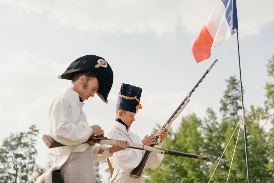 Side view of men in French military uniform charging guns against green trees during reconstruction in nature