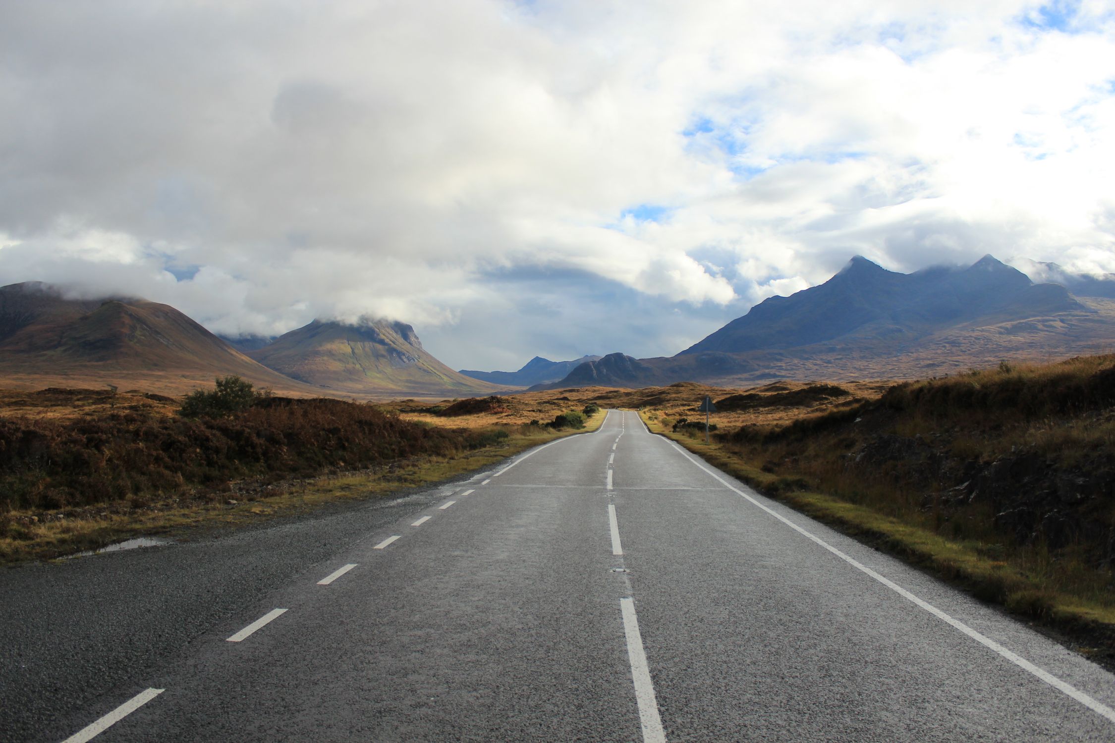 Empty road through dramatic Scottish Highlands landscape with mountains and cloudy sky.