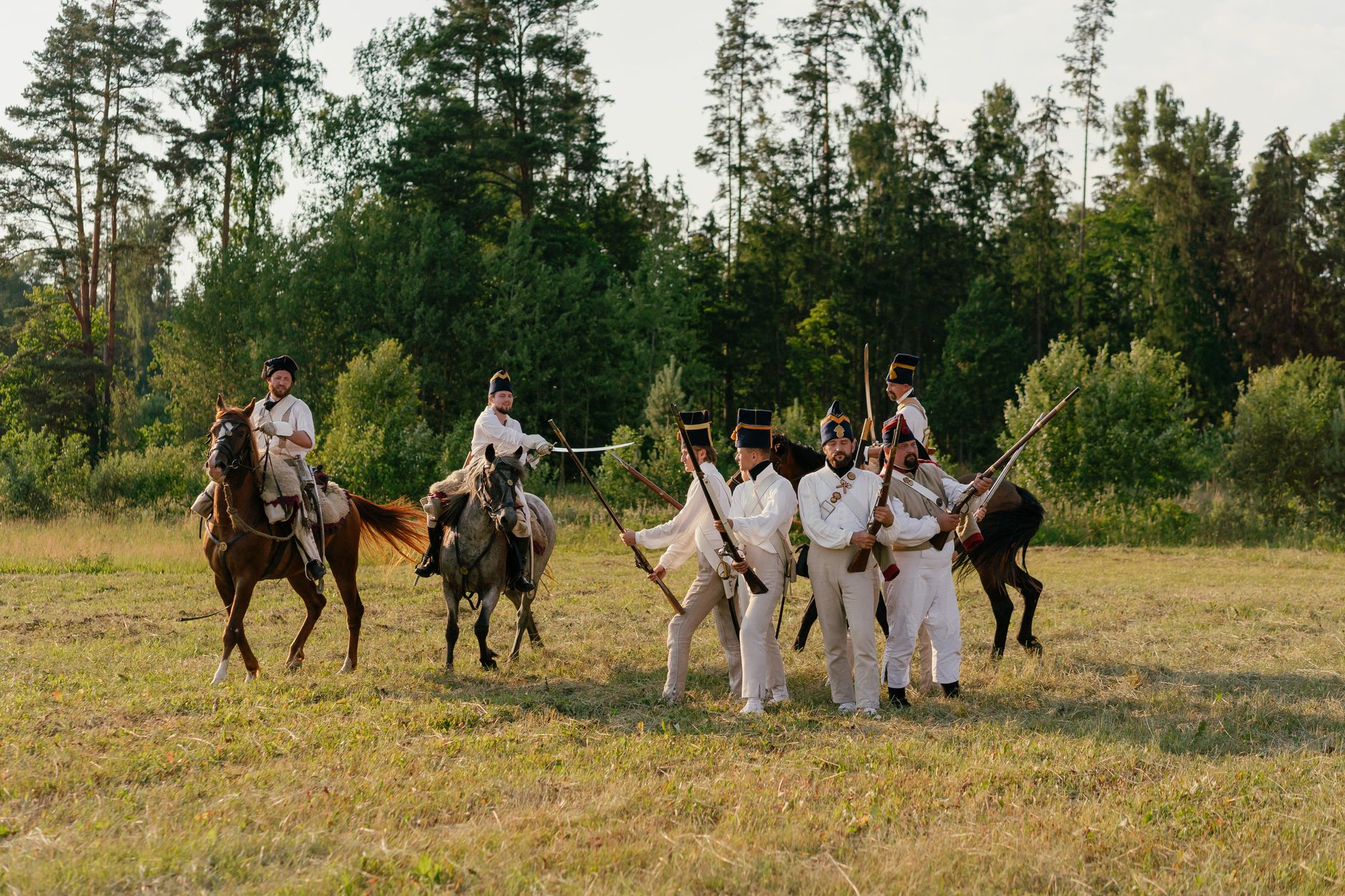 Group of men reenacting a historical military scene with soldiers on foot and horseback in a grassy field.