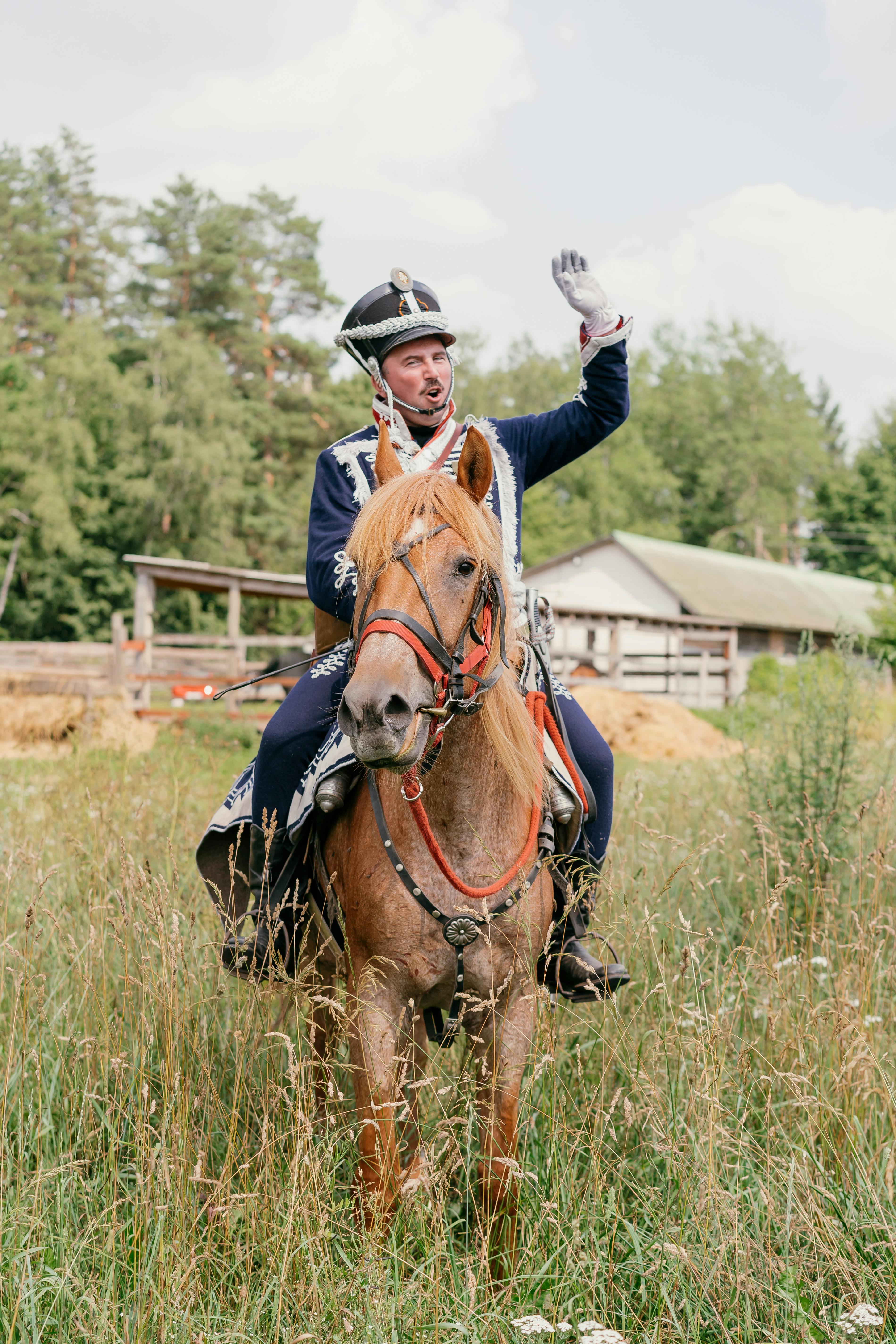 A soldier in uniform saluting while riding a horse outdoors in a rural setting.