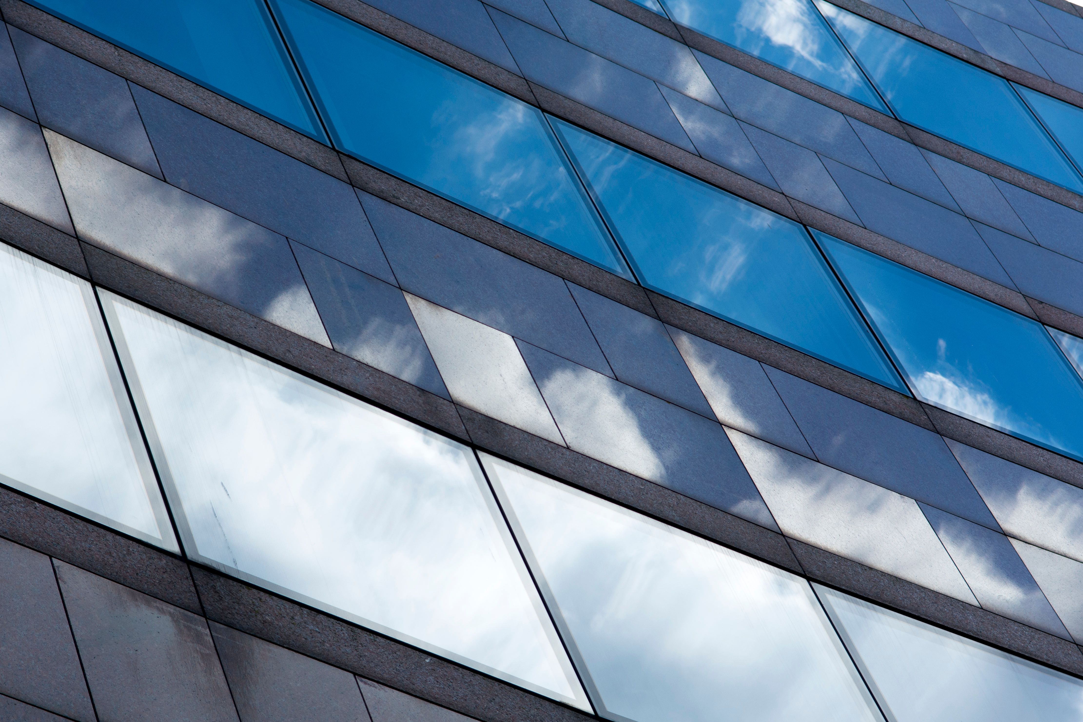 Low angle view of modern city building facade reflecting clouds in blue glass windows.