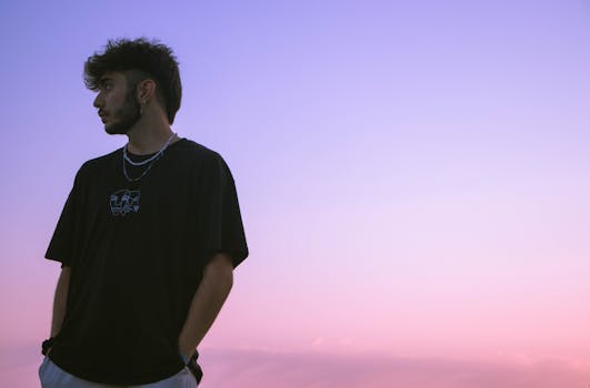 A young man is looking sideways against a pink and purple sunset sky, creating a serene and contemplative mood.