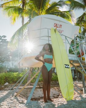 Woman in swimsuit posing with surfboard by a lifeguard tower on a sunny beach day.