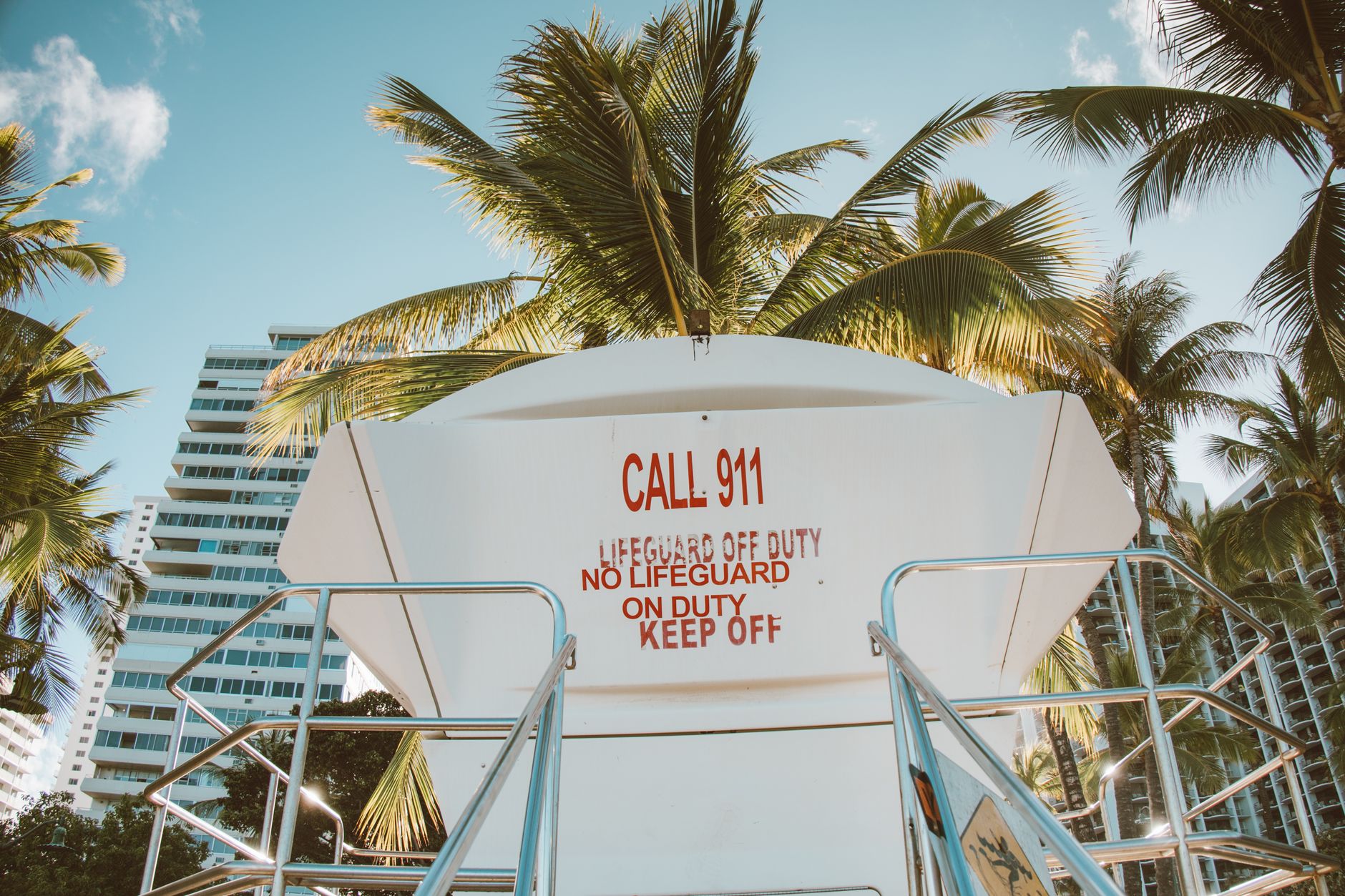 Low angle view of a lifeguard tower with a warning sign and palm trees, creating a tropical beach vibe.