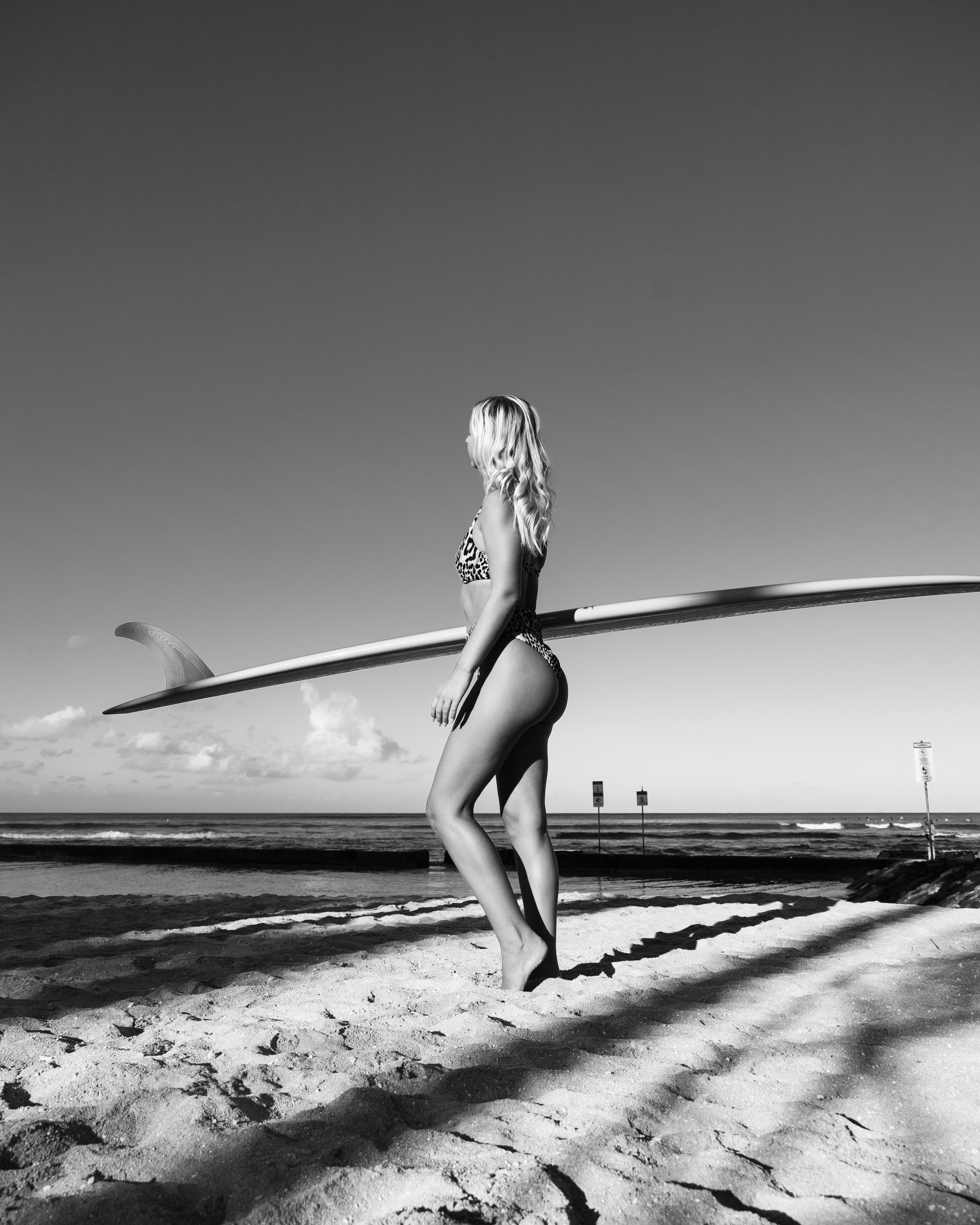Monochrome photo of a woman with surfboard on beach, capturing summer vibes.
