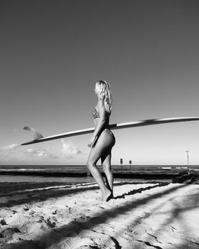 Monochrome photo of a woman with surfboard on beach, capturing summer vibes.