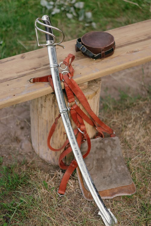 Close-up of a Sword and Leather Objects Lying on a Wooden Bench 