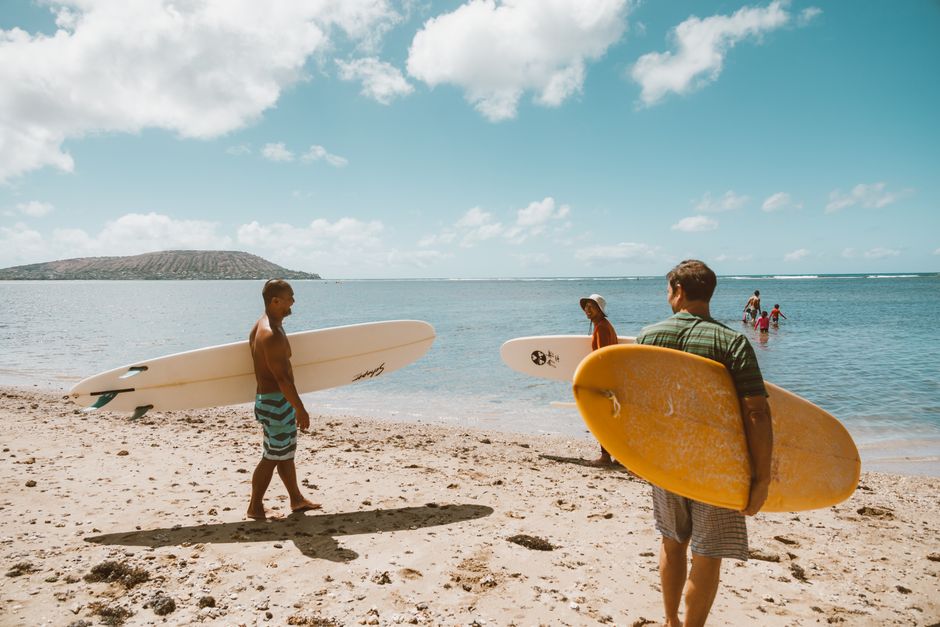 A group of surfers with boards enjoy a sunny day on a sandy beach by the ocean.