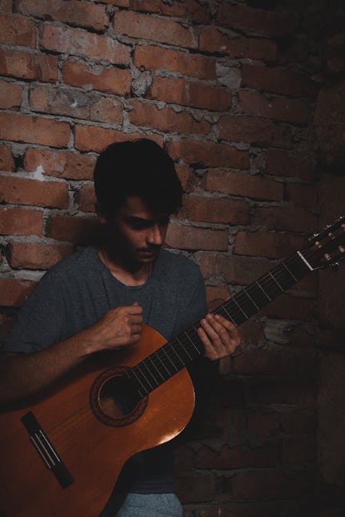 Man Holding Guitar While Standing Beside a Brick Wall