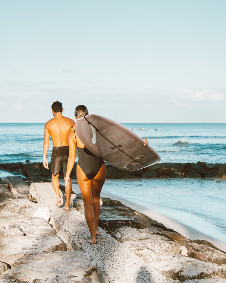 Man And Woman Walking While Carrying Surfboards