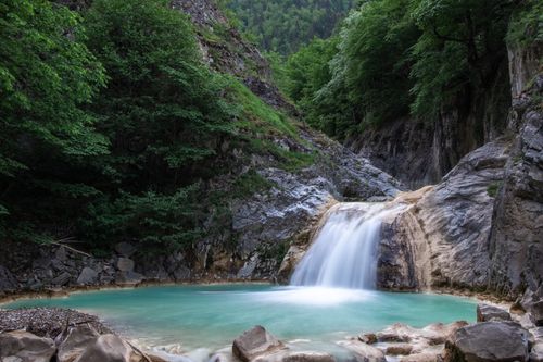 Free A tranquil waterfall flowing into a turquoise pool surrounded by lush greenery and rocky cliffs. Stock Photo