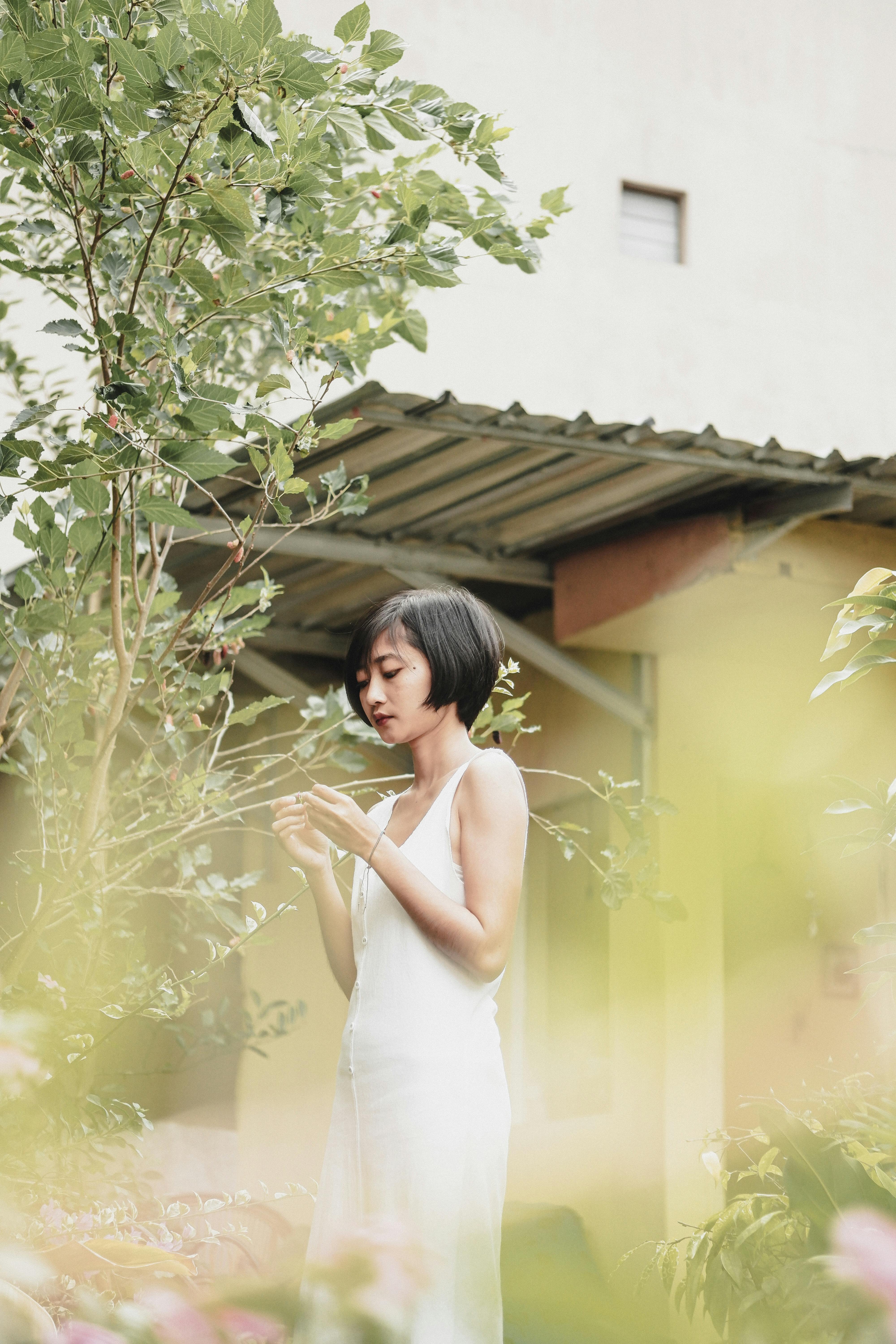 Serene portrait of an Asian woman in a white dress surrounded by lush plants.