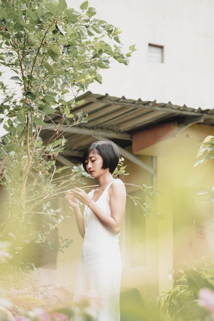Serene portrait of an Asian woman in a white dress surrounded by lush plants.