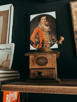 Old-fashioned coffee grinder on a shelf with portrait art in the background.