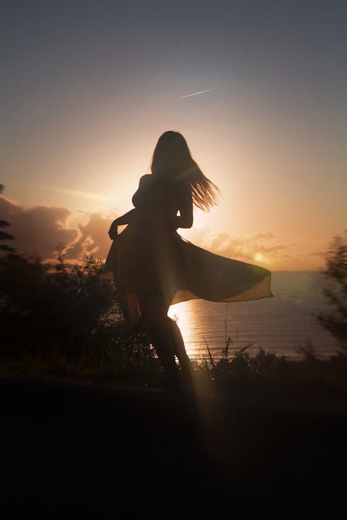 Silhouette of Woman Dancing Near Body of Water during Sunset