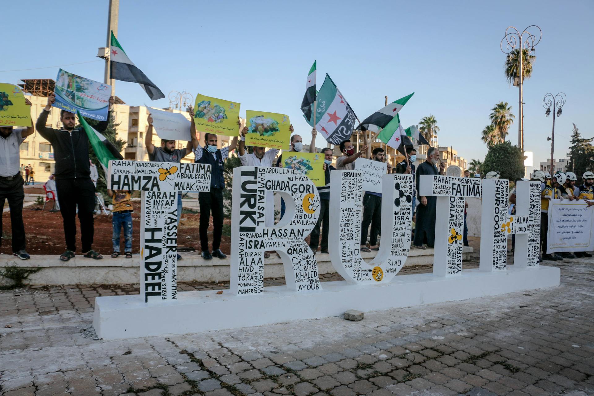 Protesters in Idlib, Syria gather with banners and flags demanding truth and justice.