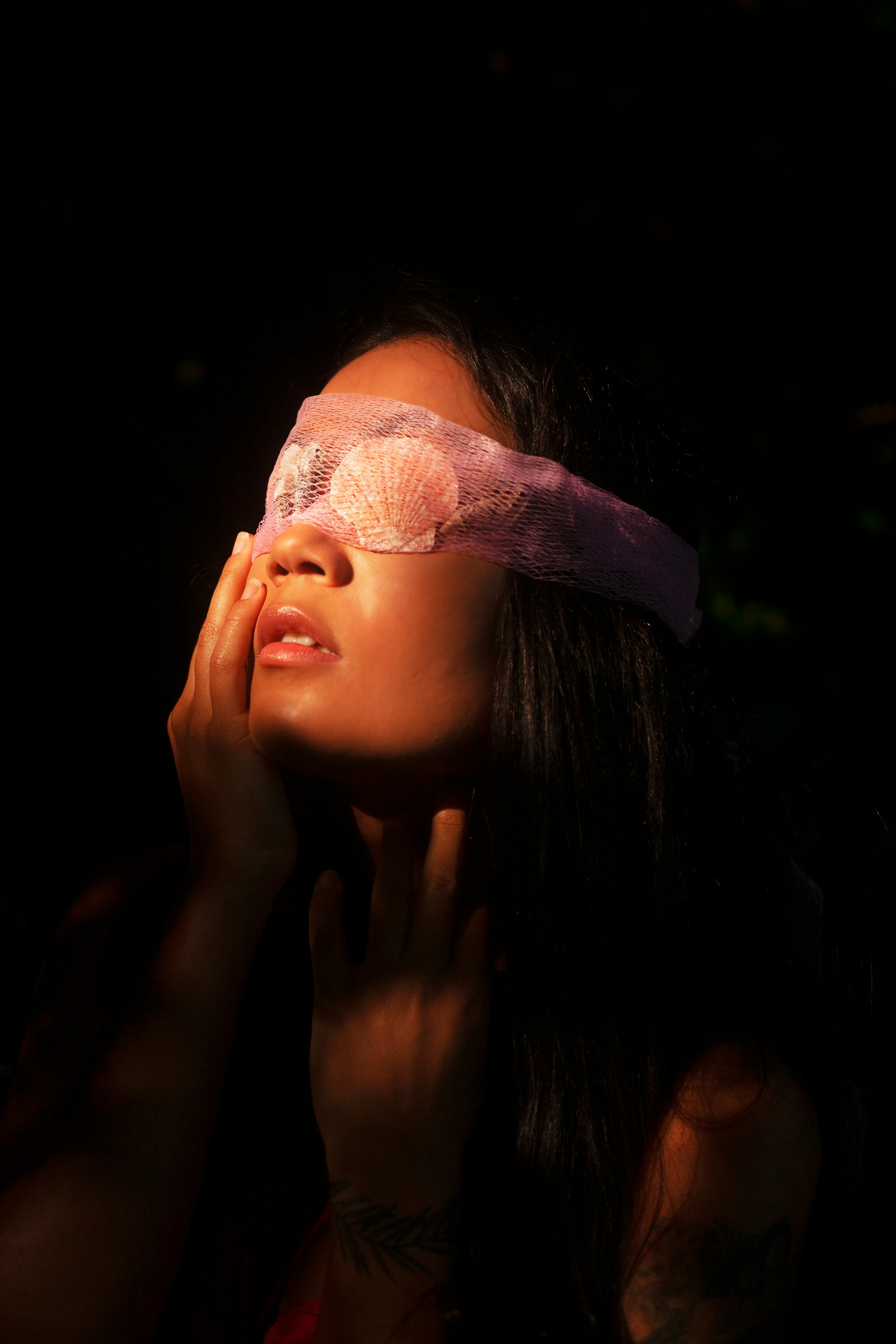 studio portrait of a young woman wearing a blindfold made of seashells and netting