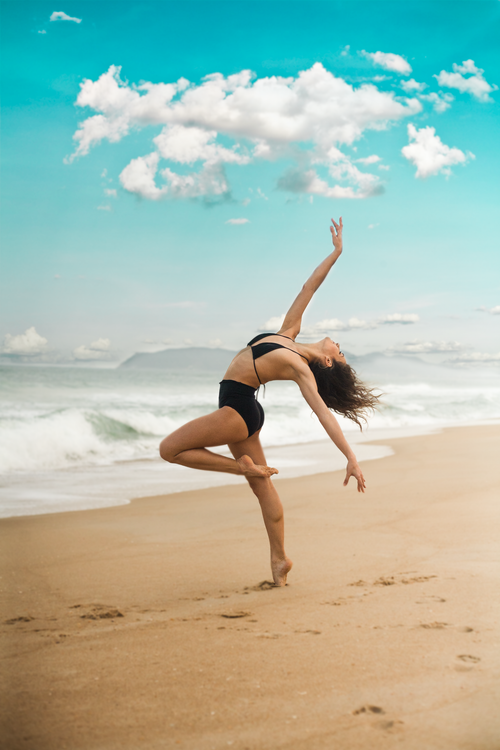 Free Woman in a black bikini gracefully posing on a sandy beach in Florianópolis, Brazil with waves in the background. Stock Photo