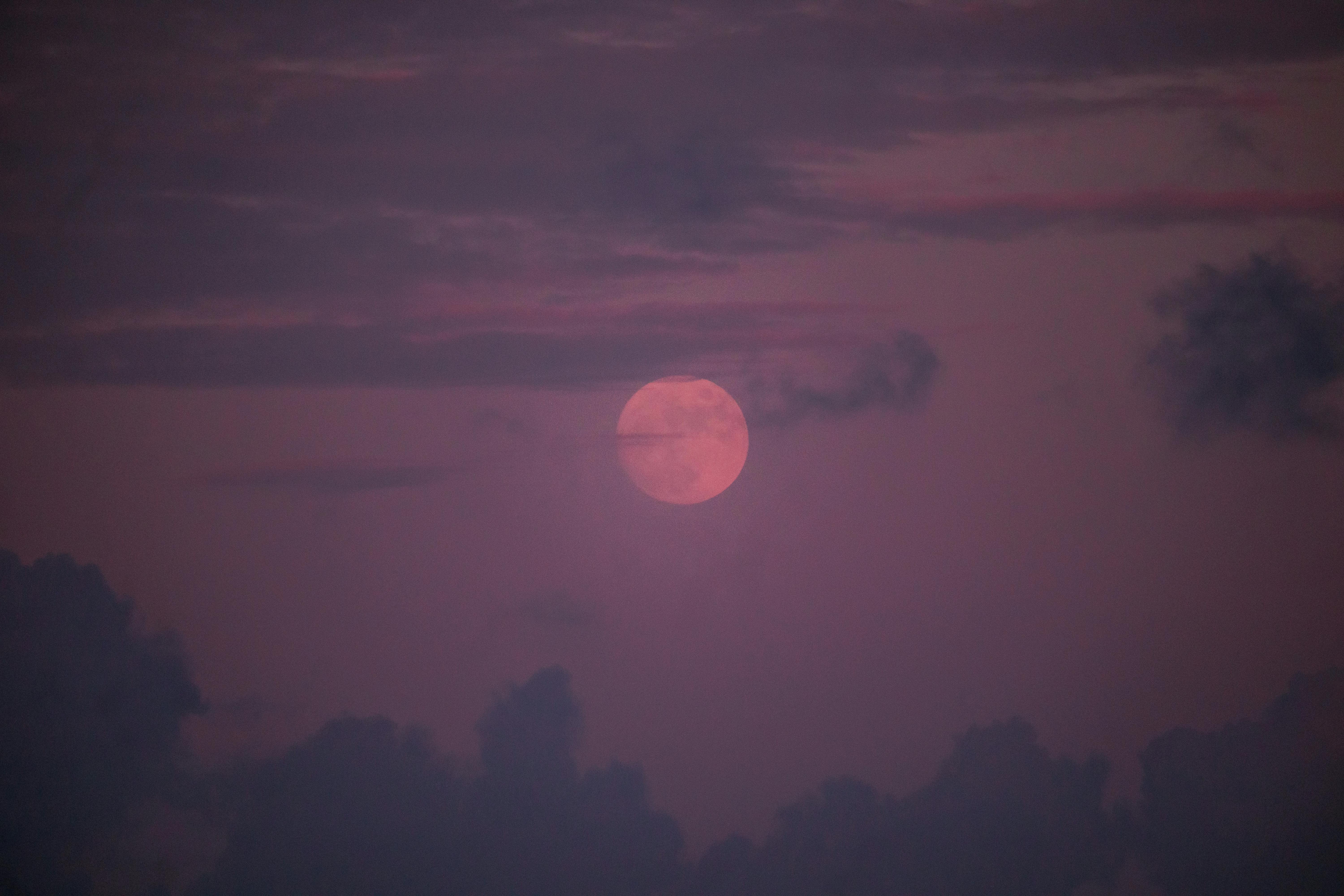 A mystical view of the moon during twilight surrounded by dark clouds.