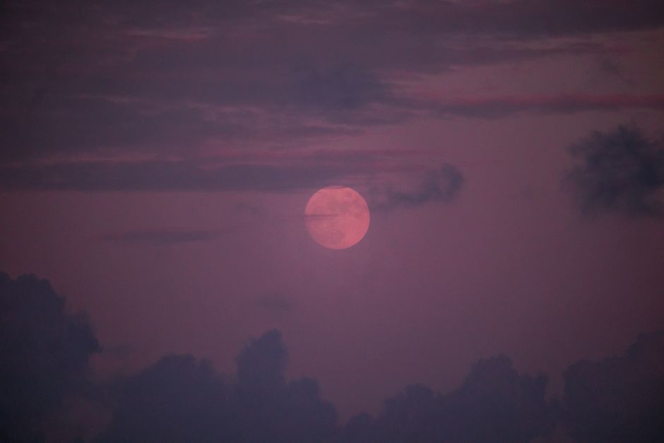 A mystical view of the moon during twilight surrounded by dark clouds.