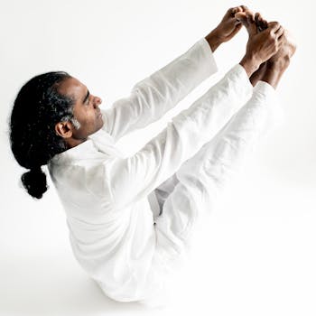 A South Asian man performing an advanced yoga pose in a minimalist white setting, demonstrating calm and focus.