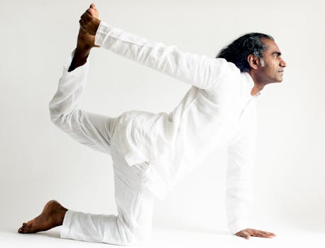 An Indian man performing a graceful yoga pose in white clothing.