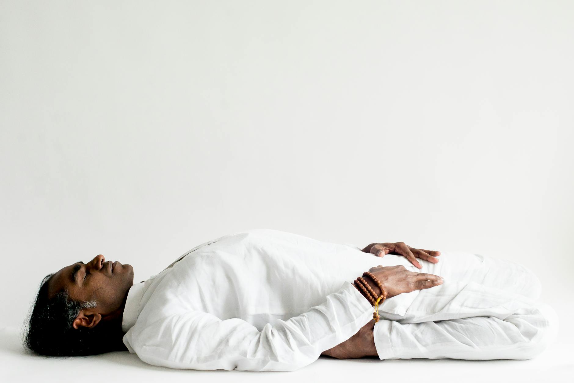 A person in a white outfit practicing meditation, lying down peacefully indoors.