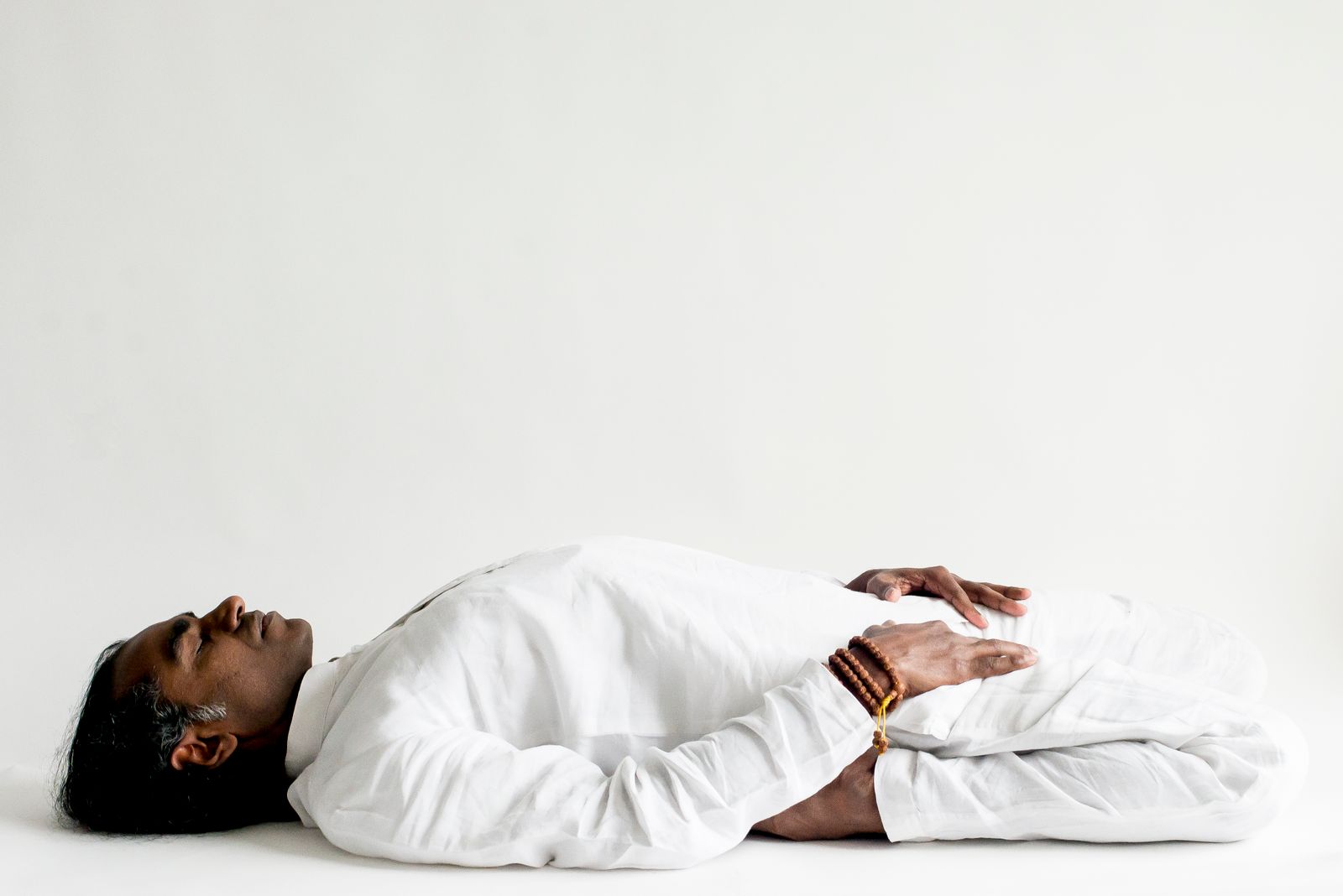 Person lying flat on their back in shavasana corpse pose with eyes closed and palms open