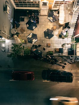 Overhead view of a bustling patio with umbrellas and street at night.