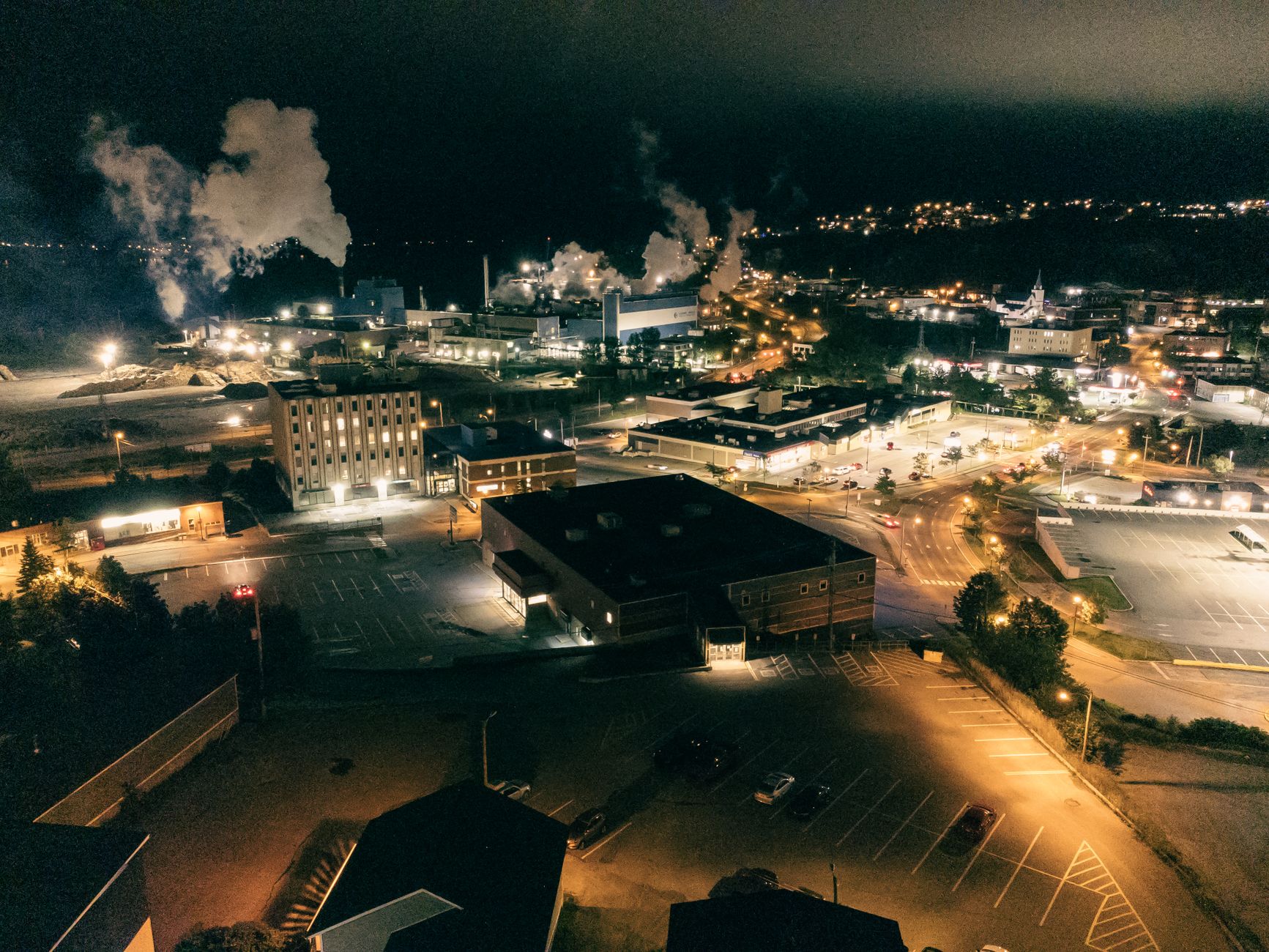 A stunning aerial night view of an industrial cityscape with glowing lights and smoke.