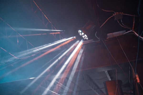 Beams of stage light cutting across a dark venue. Photo by Erik Mclean on Pexels.