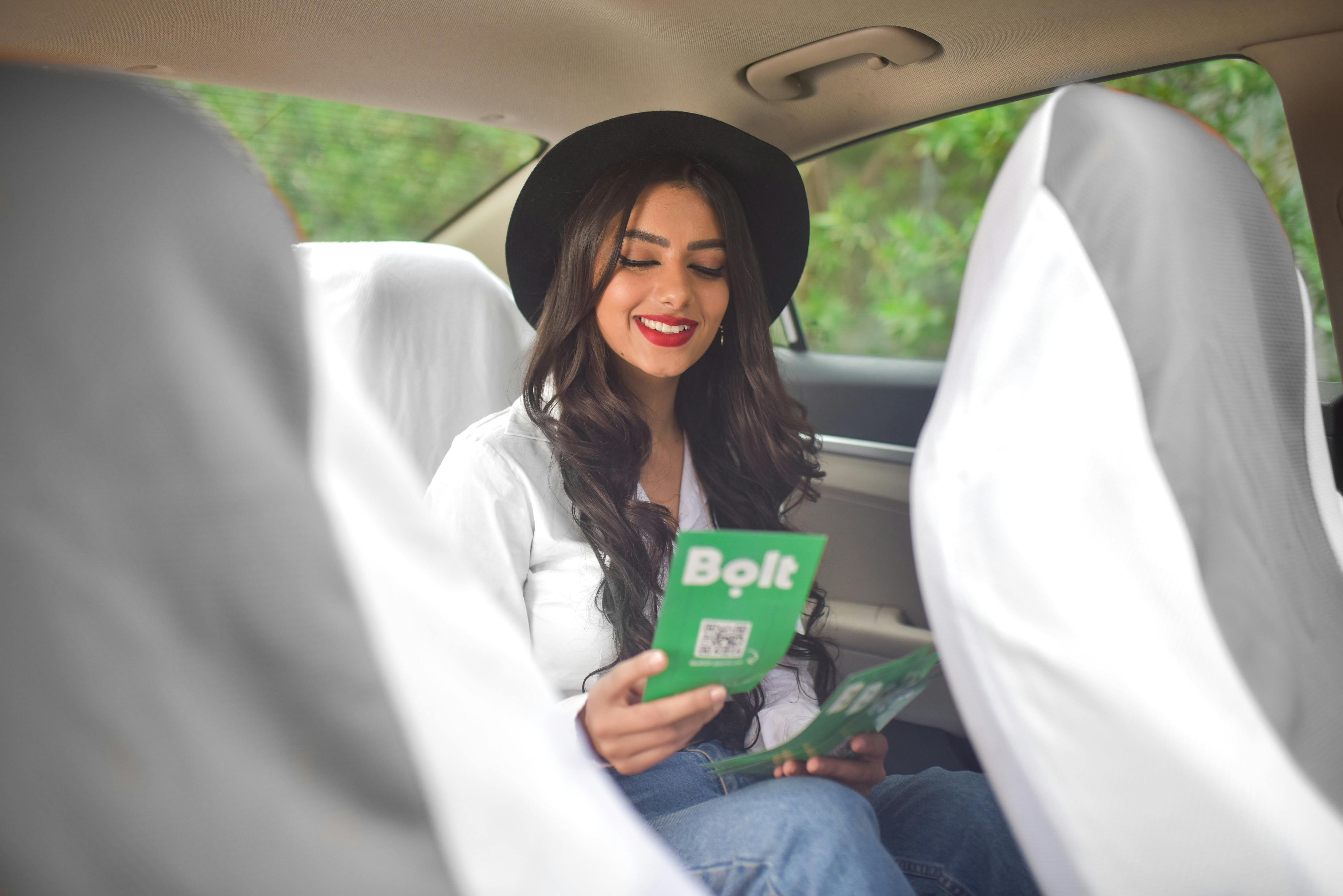 A young woman wearing a hat reads a flyer inside a car, smiling and relaxed.