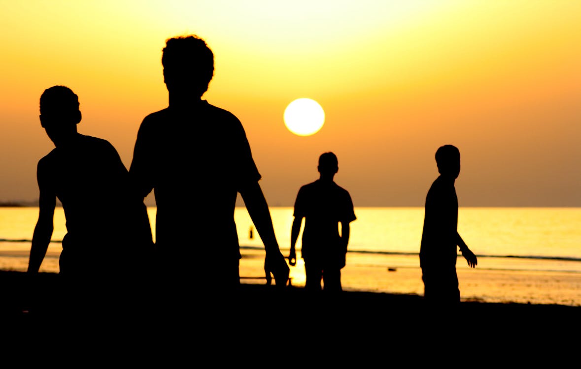 日没時の海の近くの4人のシルエット 無料の写真素材