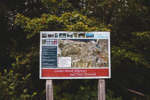 Detailed map sign for Corner Brook Bikeway and Trail Network surrounded by lush greenery.