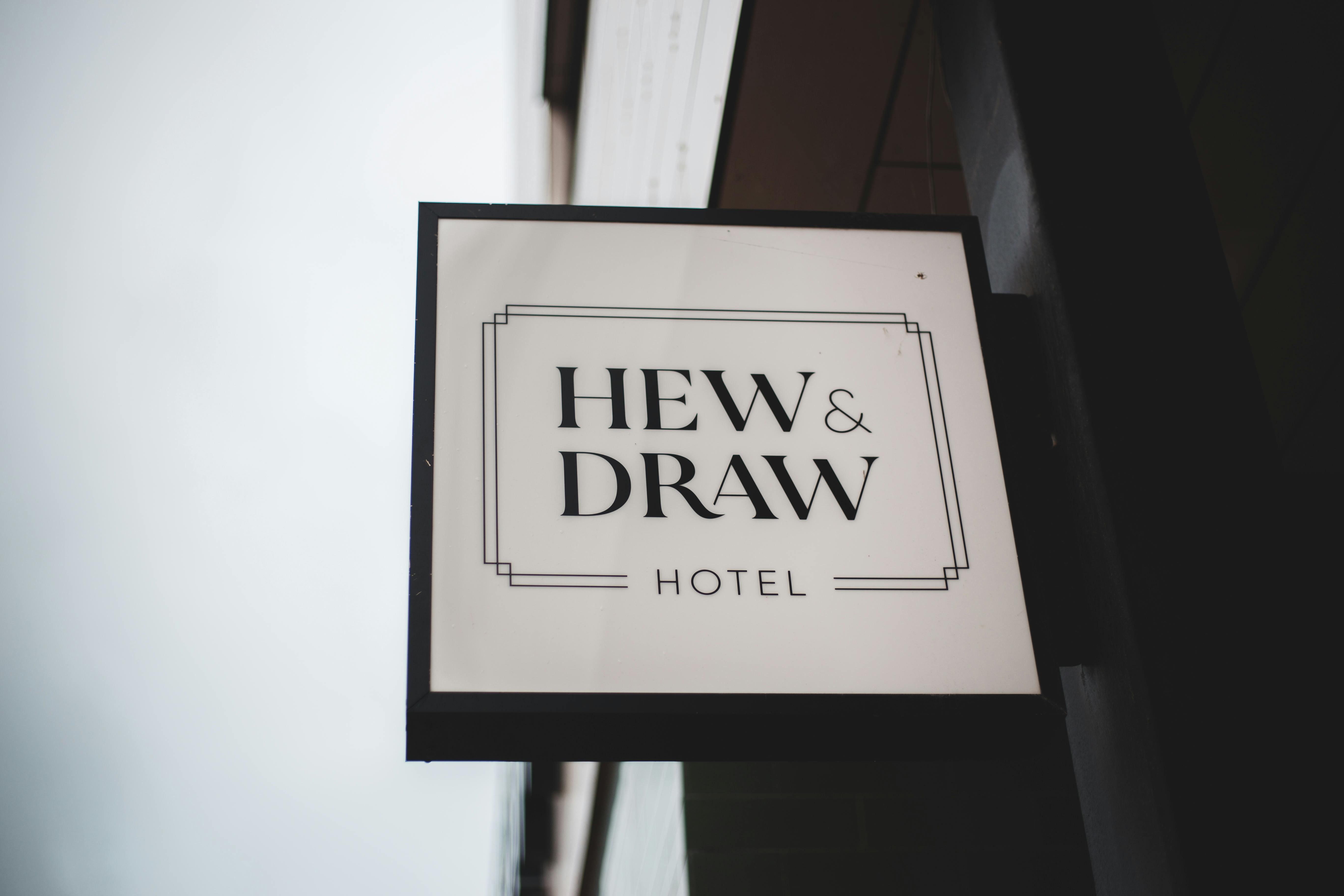 Close-up of Hew & Draw Hotel sign against a cloudy sky, showcasing modern branding.