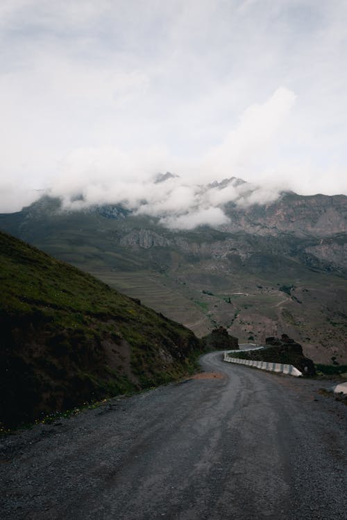Gray Concrete Road Near Mountains Under White Clouds