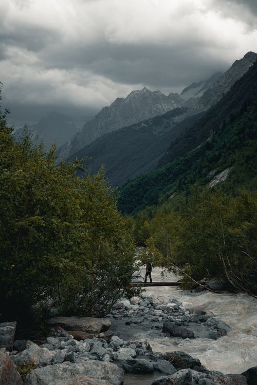 Free A lone hiker crosses a mountain stream under dramatic clouds. Perfect for nature and adventure themes. Stock Photo